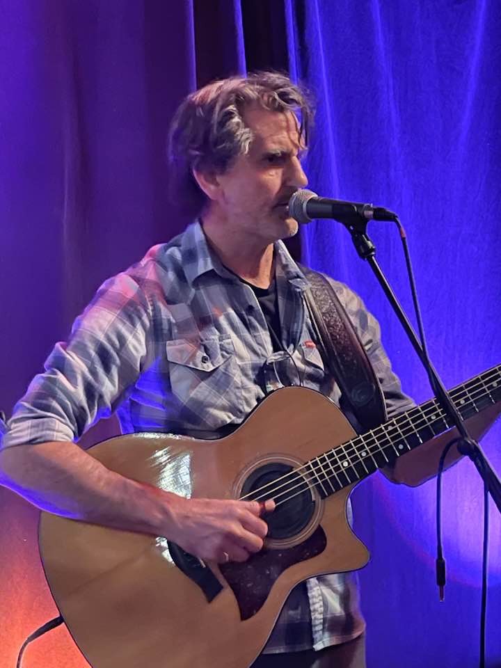 Ryan Harlock performing with acoustic guitar and microphone